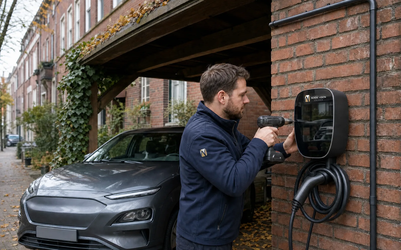Ein Elektriker montiert die Wallbox an der Klinkerwand des Carports